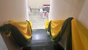 A staircase with yellow and green drapes, leading to a room with white chairs and a table. - Hotel Ashray Noida (Noida)