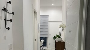 A hallway with white walls, a marble floor, and a wooden cabinet with a potted plant. - Apartment KISTO AT HOME (Bari)