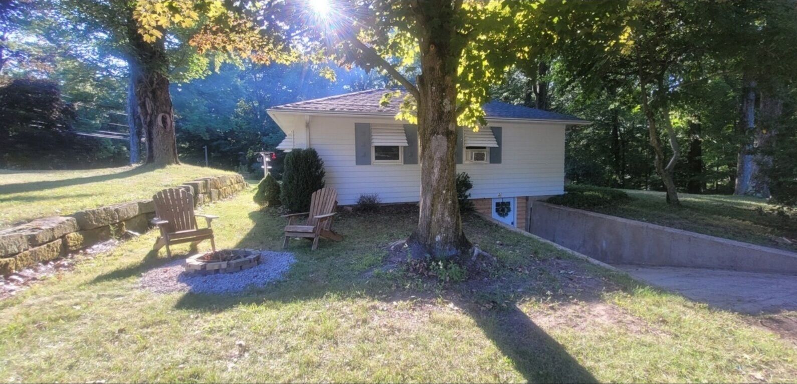 Une maison de plain-pied avec un petit jardin devant, un foyer et deux chaises en bois.