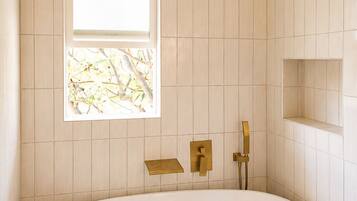 A bathroom with a freestanding bathtub, a window, and a showerhead.