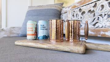 Un plateau en bois sur lequel reposent deux boîtes de conserve et deux mugs en cuivre, le tout posé sur une surface texturée.