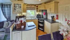 Una cocina compacta con una isla central, un comedor con mesa y sillas, y una sala de estar con sofá y una planta.
