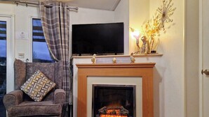 Una sala de estar acogedora con chimenea, un sillón cómodo, un televisor de pantalla plana sobre la chimenea y un adorno decorativo en la pared.