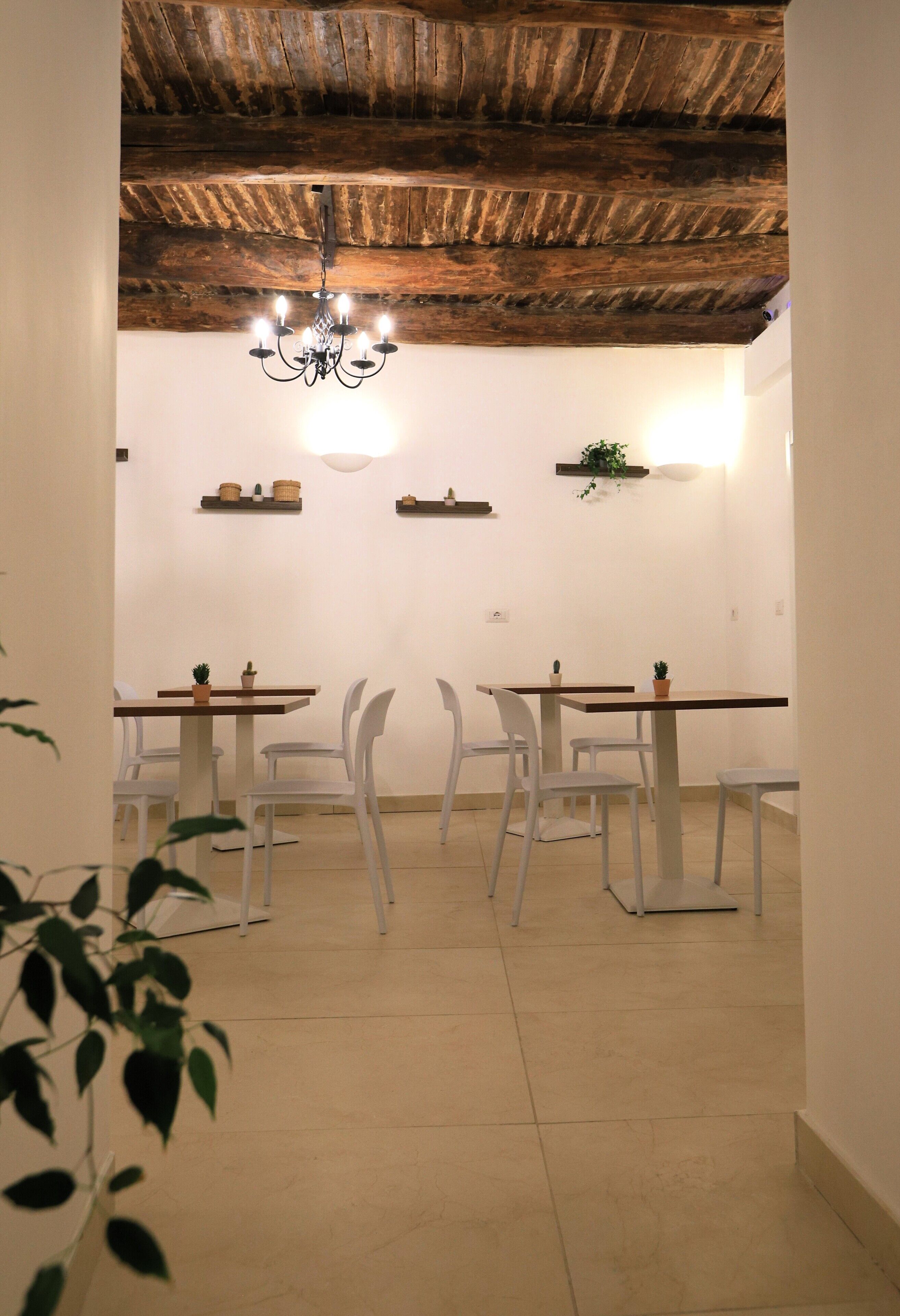 A dining area with white chairs, wooden tables, a chandelier, and shelves with decorative items.