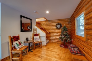 Interior acogedor de una cabaña de troncos con una escalera de madera, un árbol de Navidad y un banco decorado con cojines festivos.