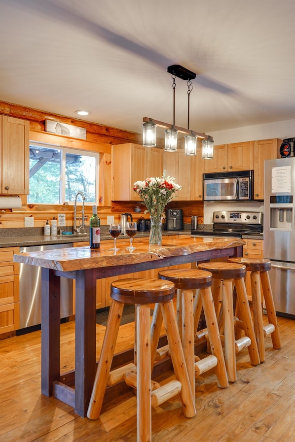 Una cocina con armarios de madera, una isla central con taburetes, electrodomésticos de acero inoxidable y una lámpara colgante.