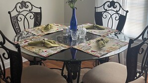 A dining table with a glass top, surrounded by four chairs with cushioned seats. A blue vase with flowers is placed in the center.