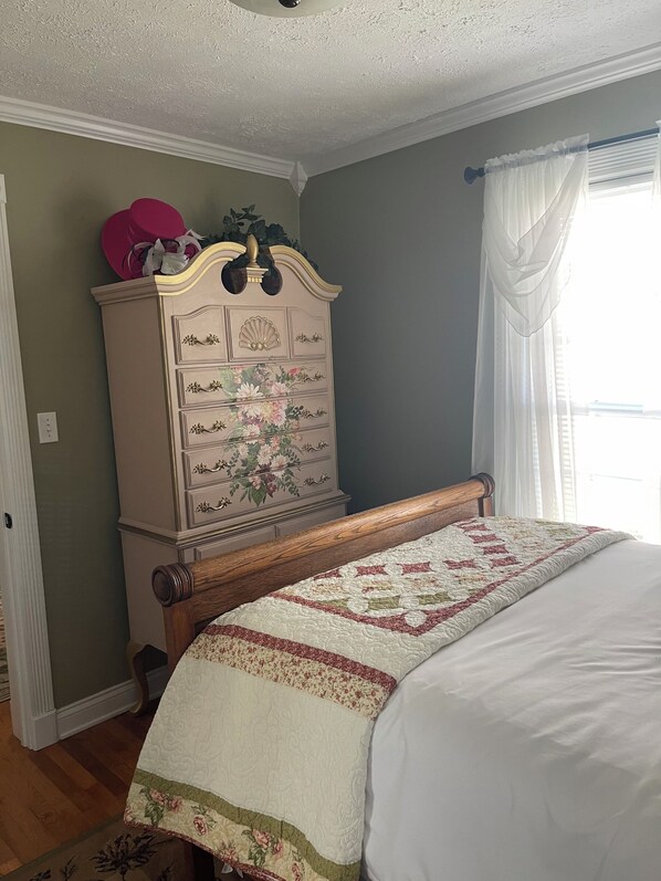 Un dormitorio con cama de madera, colcha floral, cómoda con cajones y ventana con cortinas.