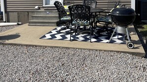 A house with a patio area featuring a grill, outdoor furniture, and a decorative rug.
