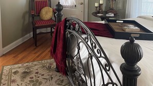 A bedroom with a bed, a chair, a side table, a lamp, a ceiling fan, and a window with curtains.