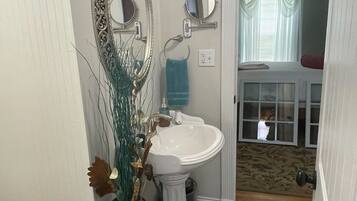 A bathroom with a pedestal sink, a large ornate mirror, and a vase with dried plants.