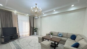 Ein Wohnzimmer mit Sofa, Hocker, Couchtisch, Fernseher und einer Chandelier.