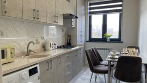 Eine moderne Küche mit integriertem Waschmaschinenanschluss, ein Essbereich mit Tisch und Stühlen sowie ein Fenster mit Stadtblick.