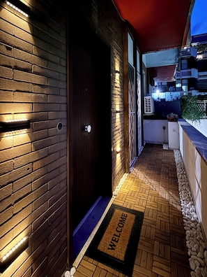 A dark wooden door with a 'WELCOME' mat, a brick wall, and a tiled floor.