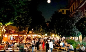 A crowded outdoor dining area with tables and chairs, surrounded by trees and buildings.