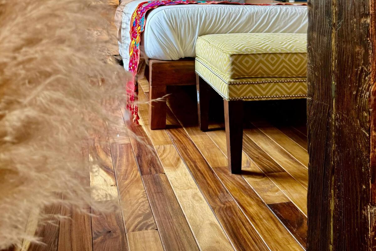 Een slaapkamer met een houten vloer, een bed met een kleurrijk hoofdeinde en een nachtkastje.