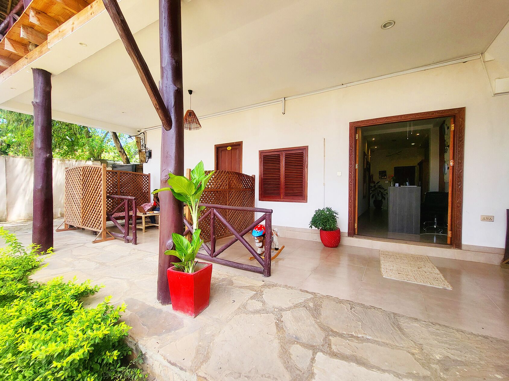 A covered outdoor area with stone flooring, wooden furniture, and potted plants.