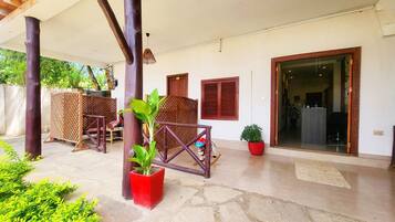 A covered outdoor area with stone flooring, wooden furniture, and potted plants.