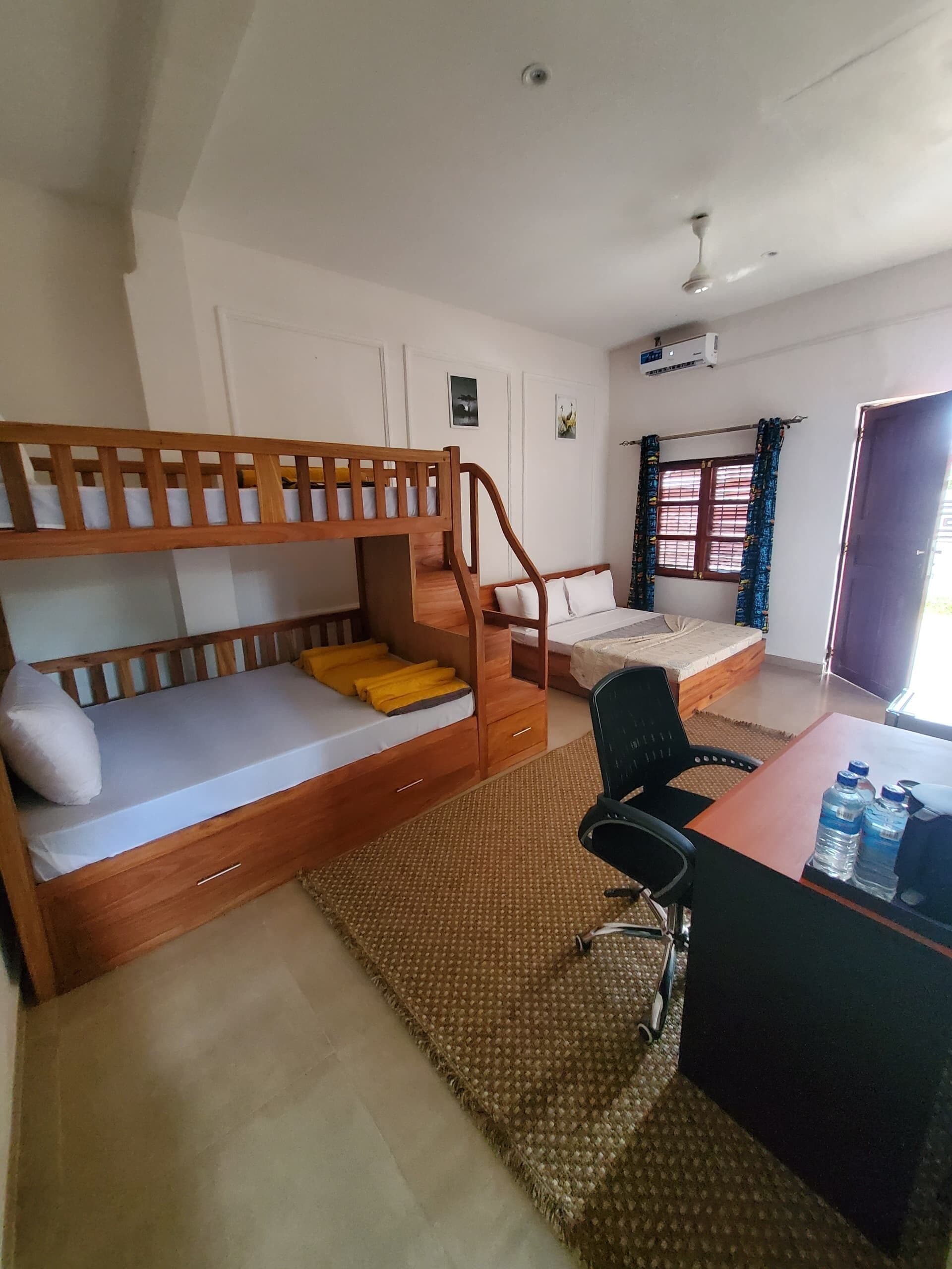 A room with a bunk bed, a desk with two water bottles, a chair, and a window with curtains.