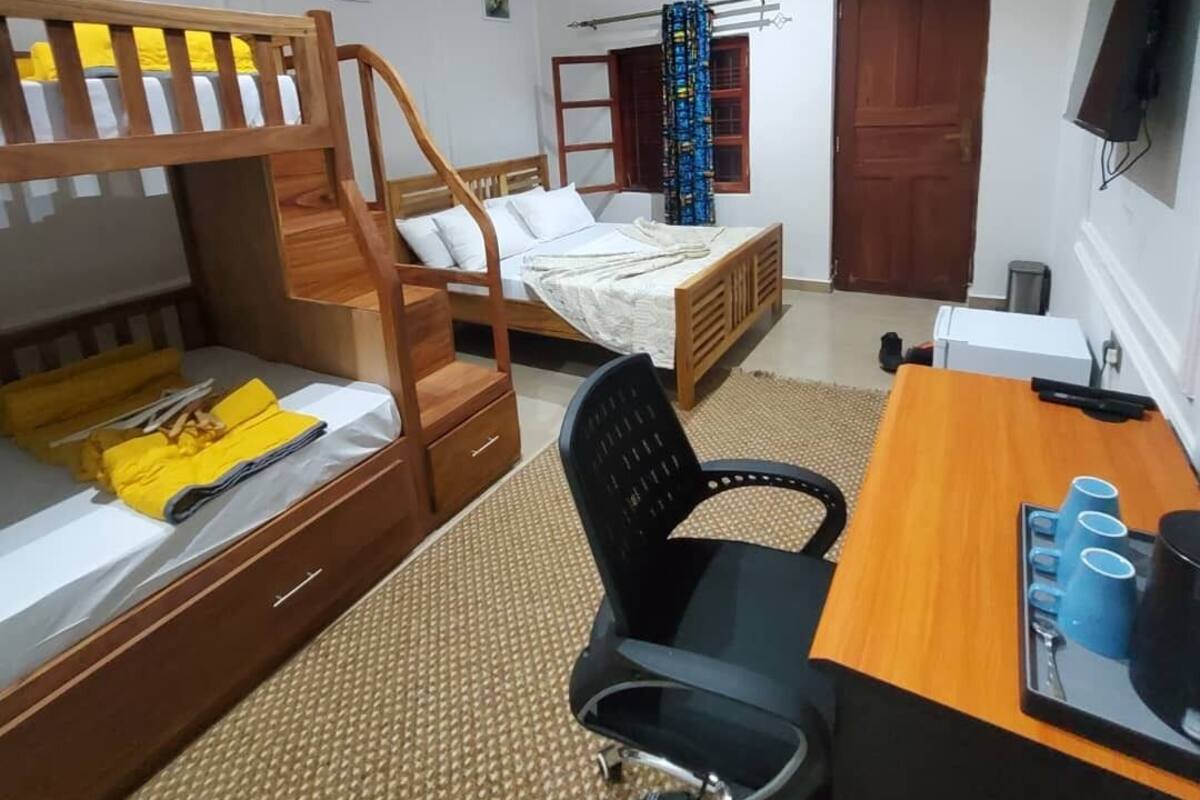 Un dormitori amb una llitera, un escriptori amb una cadira, una televisió i un ventilador de sostre.