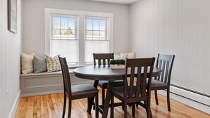 Un comedor con una mesa redonda y seis sillas, un banco con cojines y una ventana con persianas.