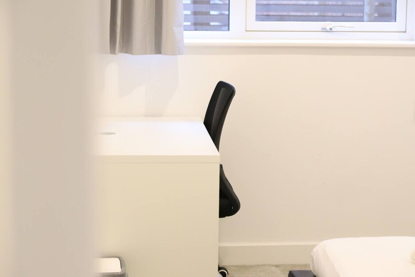 A small, white room with a desk, chair, and a window with blinds.