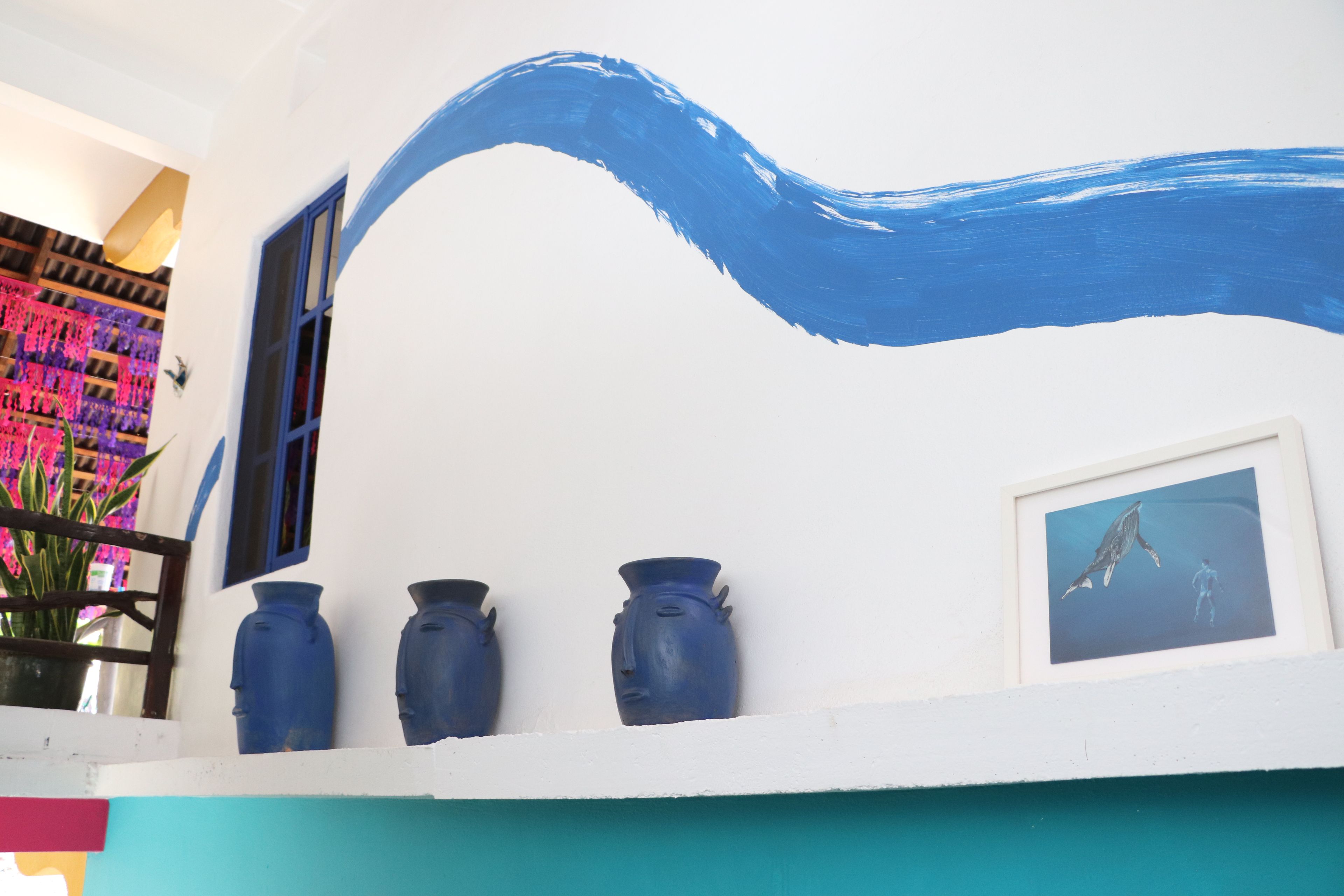 A white building with a blue wave painted on the wall, three blue vases on the balcony, and a framed picture of a whale.
