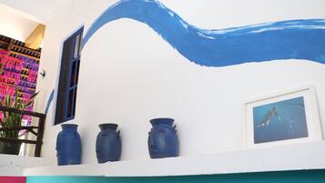 A white building with a blue wave painted on the wall, three blue vases on the balcony, and a framed picture of a whale.