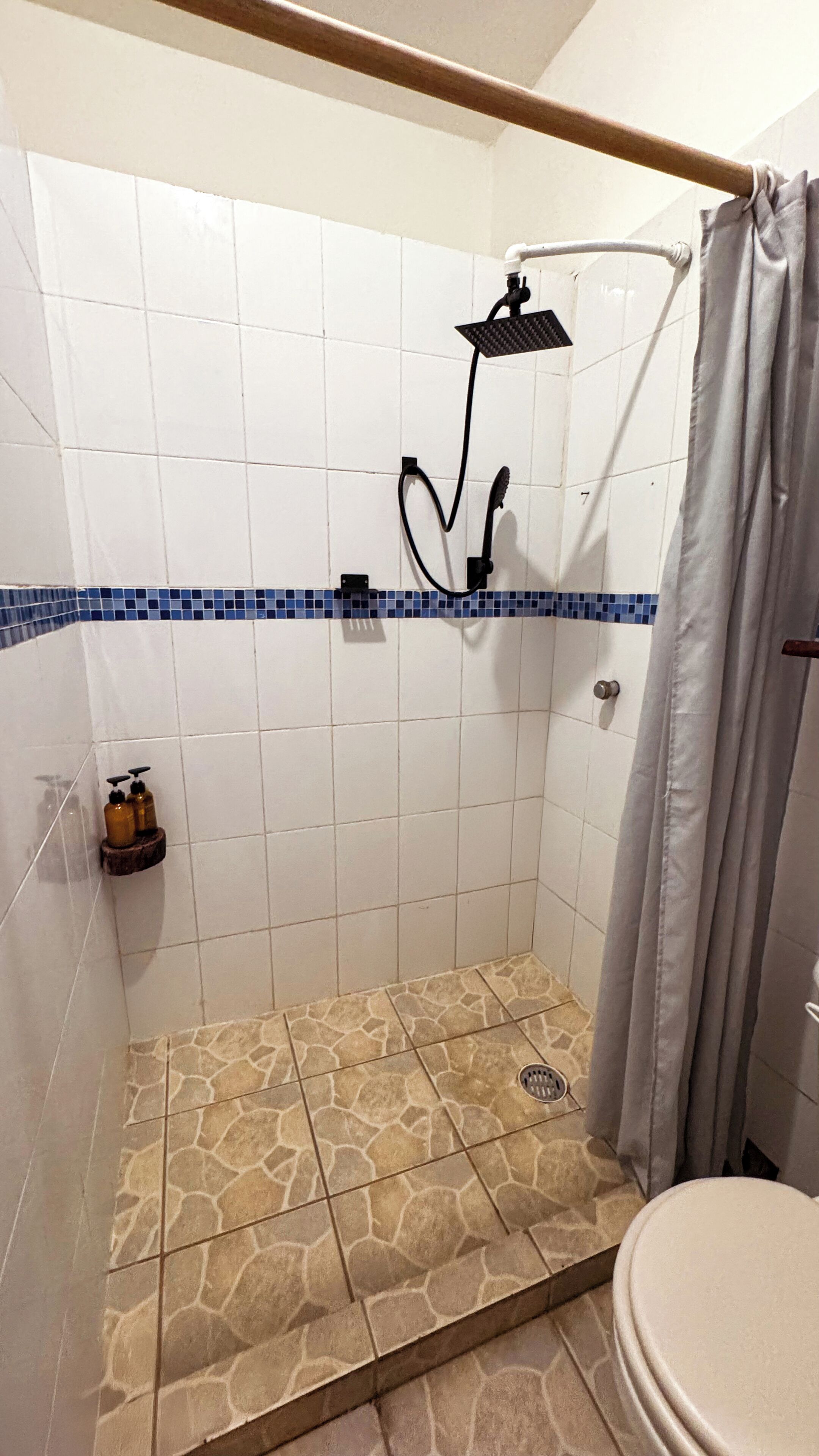Un área de ducha con ducha de lluvia, desagüe y suelo de baldosas.