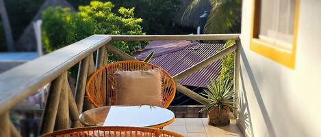 Un balcón con mesa y sillas naranja, con vista a un jardín de palmeras.