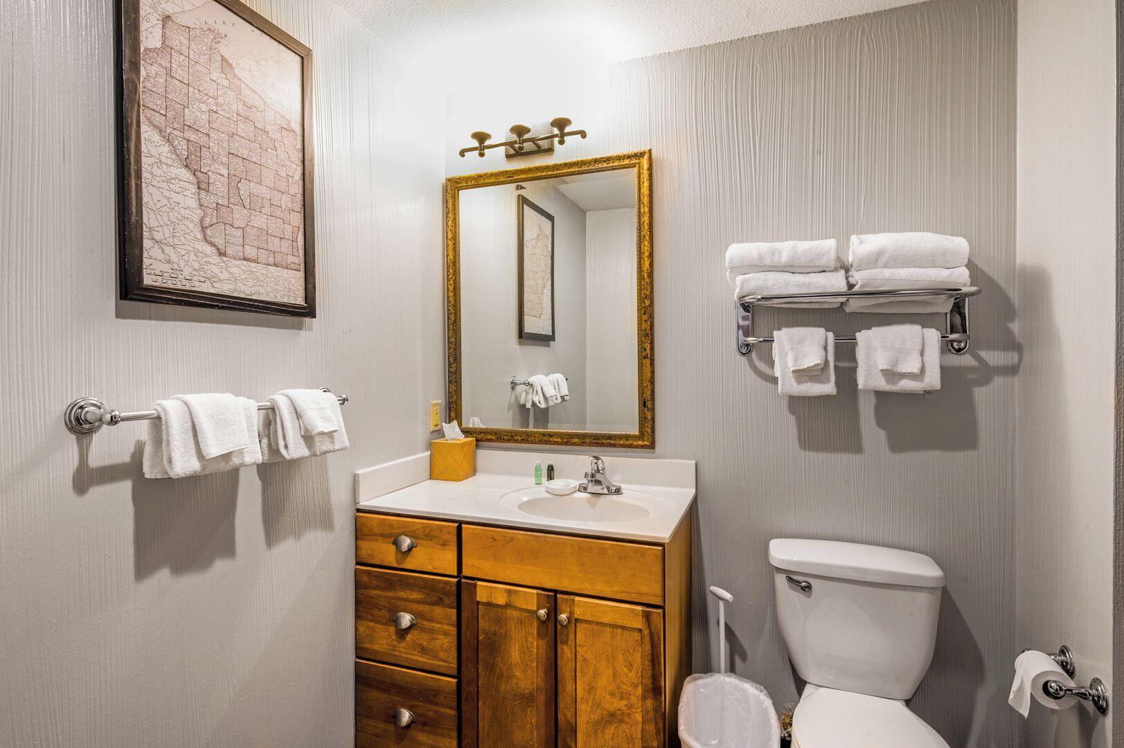 Une salle de bain avec un meuble-lavabo en bois, un grand miroir avec un cadre doré, des toilettes et un porte-serviettes avec des serviettes pliées.