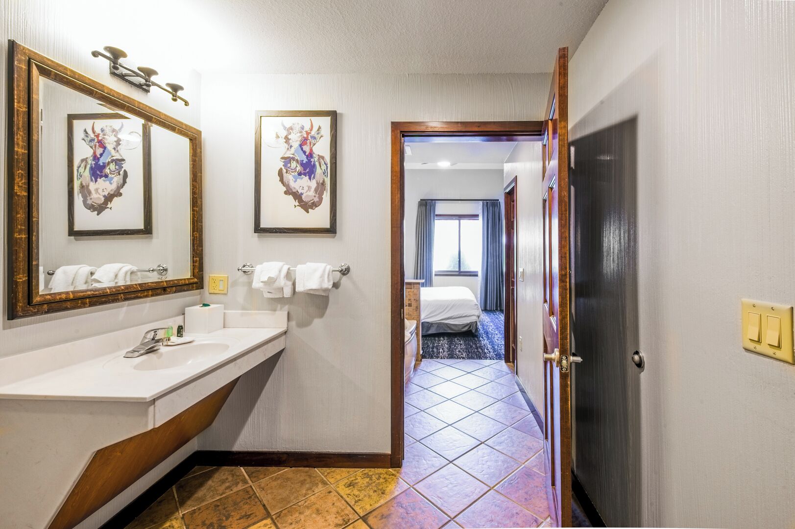 A hotel bathroom with a sink, mirror, and two framed artworks.