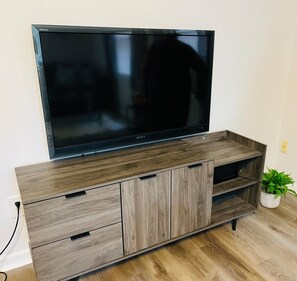 Un téléviseur à écran plat posé sur un meuble télé en bois, avec une plante à côté.