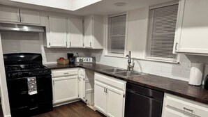 A kitchen with white cabinets, a black stove, a stainless steel sink, and a dishwasher. - The Amazing 4 Bed 2 Bath of Independence (Independence)