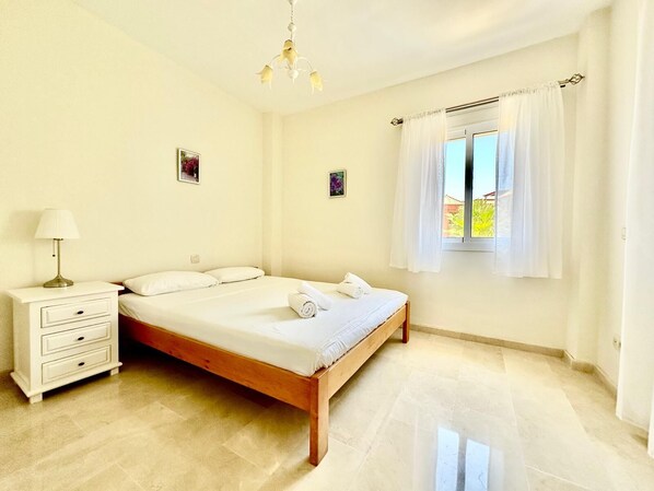 A bedroom with a bed, a nightstand, a lamp, and a window with curtains. - Casa Princesa Kristina (Manilva)