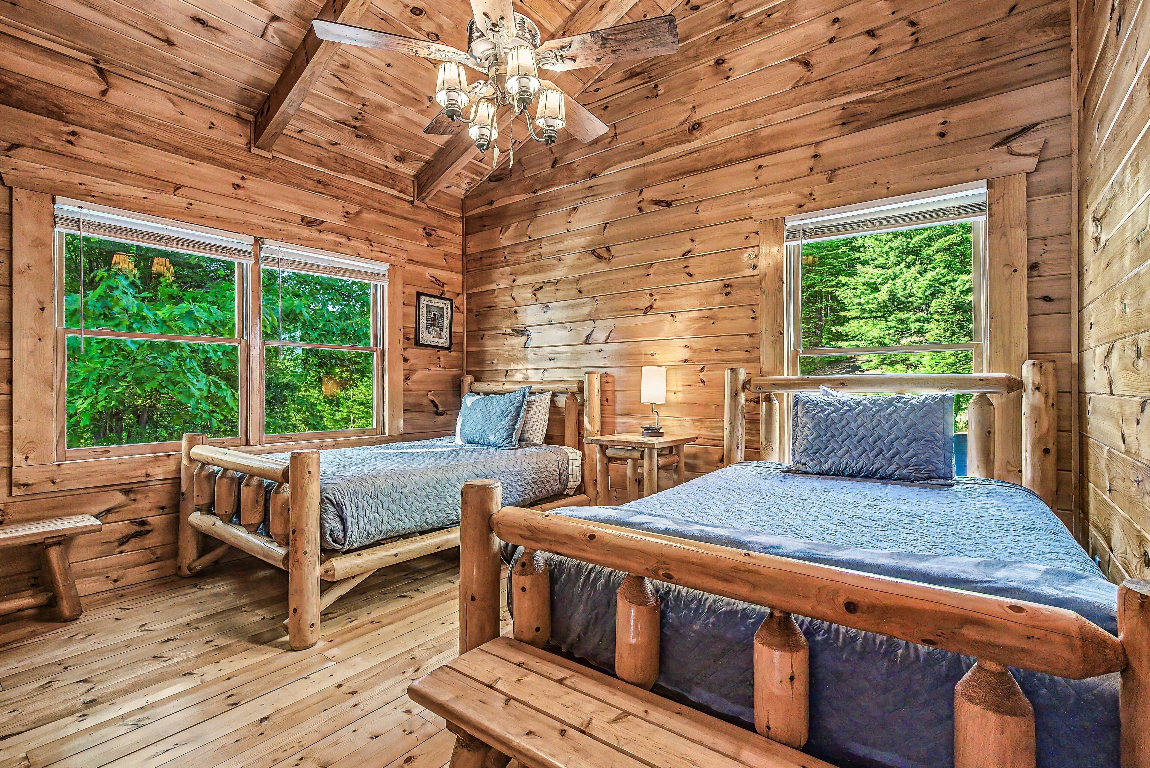 Une cabane avec deux lits en bois, un ventilateur de plafond et de grandes fenêtres.