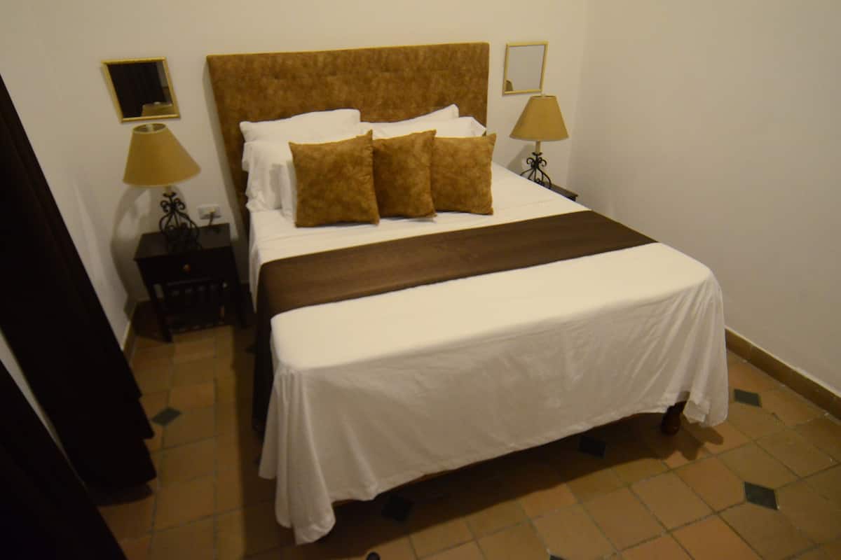 Habitación de hotel con una cama grande, dos mesitas de noche, un tocador, un espejo y una lámpara.