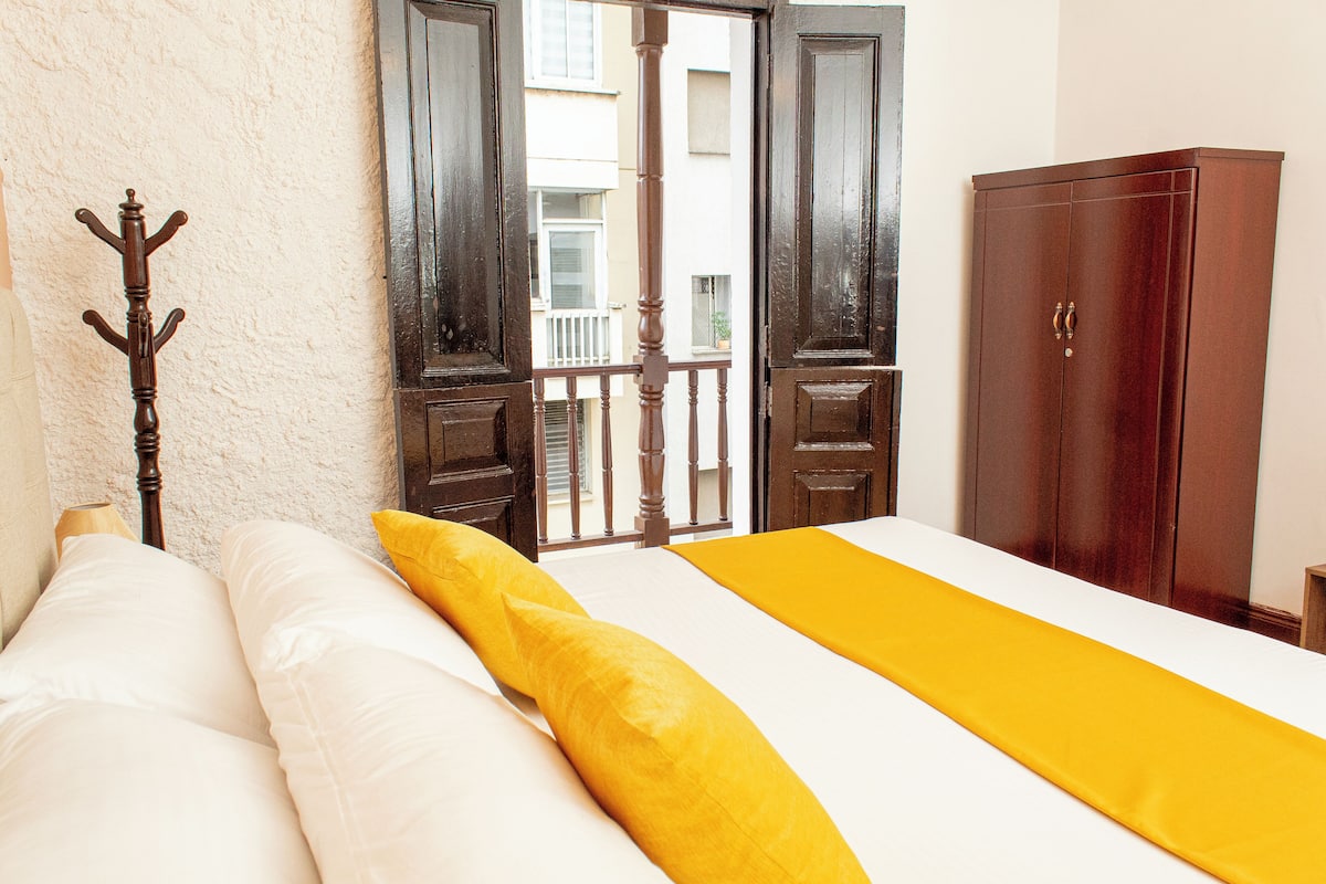 Un dormitorio con una cama, un armario de madera y un balcón visible a través de la puerta abierta.