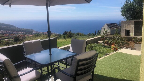 An outdoor seating area with a table and chairs, an umbrella, and a view of the sea. - Casa Jardim Panoramic View (Estreito da Calheta)