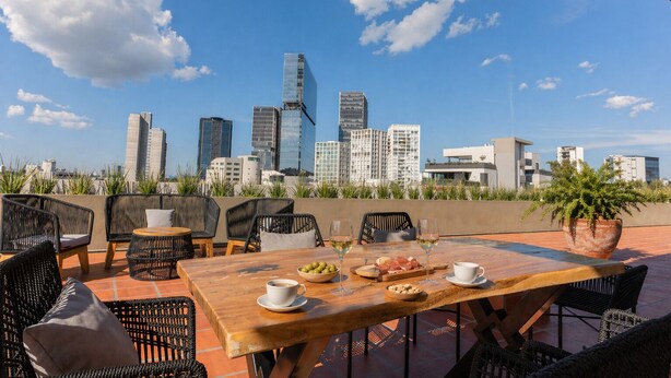 A rooftop terrace with a city skyline view, outdoor seating with wicker chairs and a wooden table, and a potted plant. - Stylish Sky Suite /Daily Clean (Guadalajara)