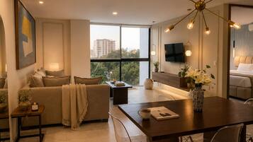 A modern living room with a sofa, coffee table, and dining area, a TV mounted on the wall, and a large window with a city view.