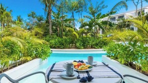 A poolside dining area with a table set for two, surrounded by lush tropical plants and a clear blue sky. - Super Studio Laguna C 106 (Tulum)
