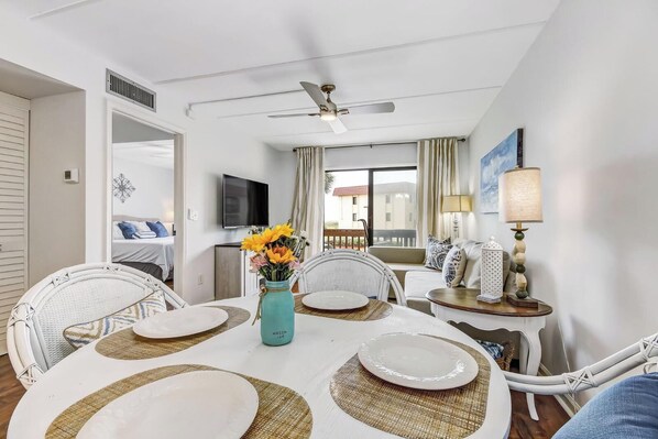 A dining area with a round table set for four, white chairs, a vase with flowers, and a ceiling fan.