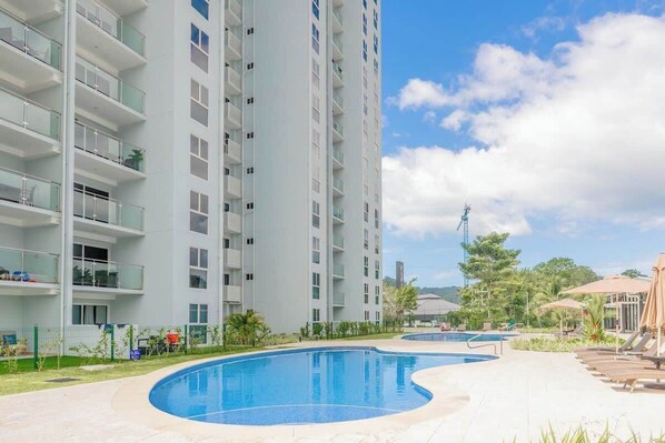 Un hotel moderno con piscina, varios balcones y cielo despejado.