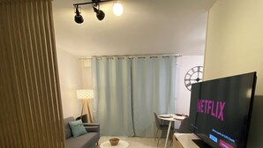 A modern hotel room with a bed, a sofa, a small round table with a bowl, a TV displaying Netflix, a lamp, and a clock on the wall. - Le Girouard - Centre - Free Parking - NETFLIX, WIFI (Poitiers)