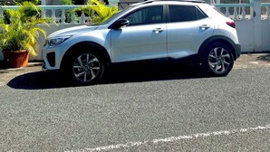 Un SUV bianco parcheggiato di fronte a una casa con tetto rosso, immersa nel verde sotto un cielo azzurro.