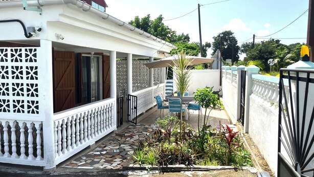 Un'area esterna riparata con pavimento piastrellato, una recinzione bianca e un piccolo giardino con piante.