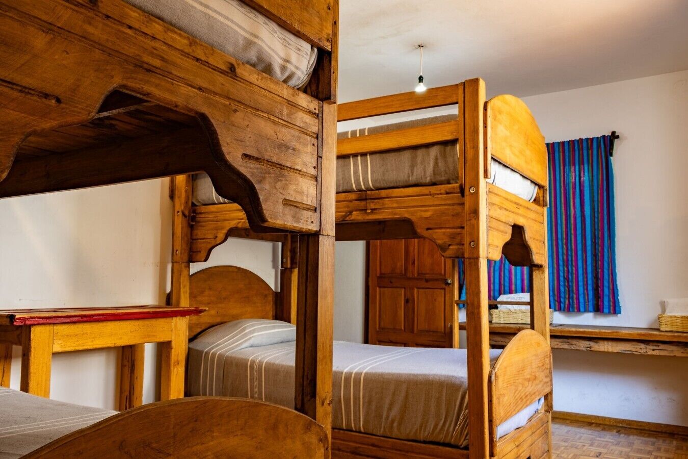A bunk bed room with a wooden headboard, a small table, and a window with a striped curtain.
