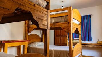 A bunk bed room with a wooden headboard, a small table, and a window with a striped curtain.