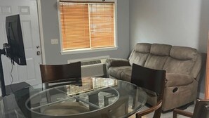 A dining area with a glass table surrounded by chairs, a ceiling fan, a window with blinds, and a gray wall.